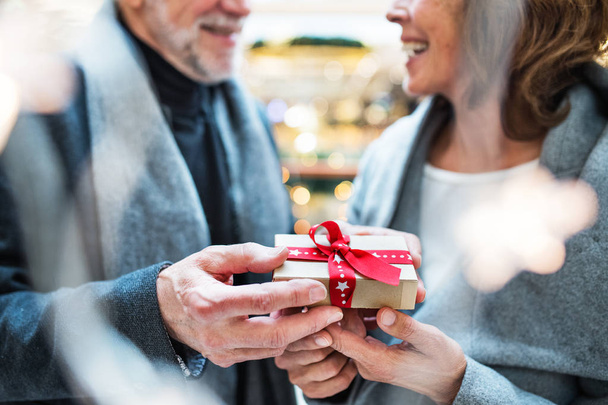 Um casal idoso irreconhecível com um presente no shopping center na época do Natal
. - Foto, Imagem