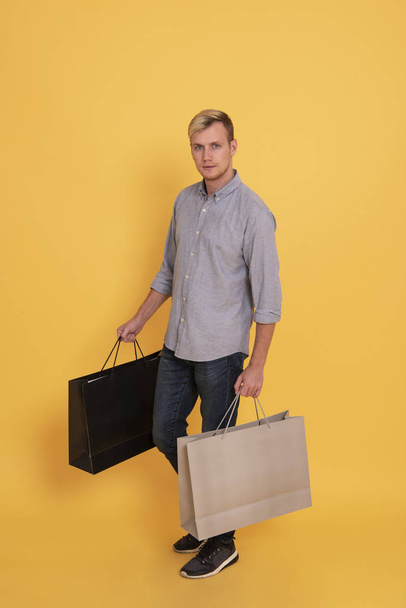 Πορτρέτο όμορφος άνδρας κρατώντας ψώνια χαρτί τσάντα πάνω από το κίτρινο φόντο. - Φωτογραφία, εικόνα