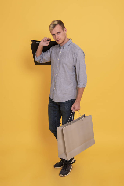 Portrait handsome man holding shopping paper bag over yellow background. - Valokuva, kuva
