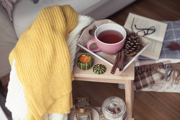 Kötött, meleg pulóverek, egy csésze forró tea, őszi dekoráció, egy könyv, egy tök, egy fából készült szék. Hangulatos, őszi dekoráció. Őszi, belső, kanapé. Esik. Téli. - Fotó, kép
