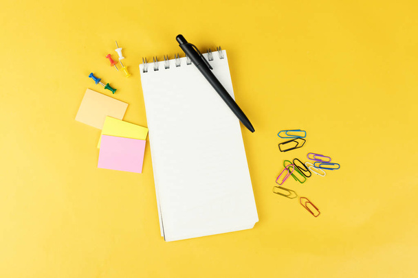 Draufsicht auf leeres Notizbuch und Schulmaterial wie farbige Marker, Aufkleber und Cliper auf gelbem Hintergrund.  - Foto, Bild