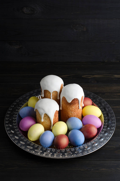 Easter still life on a dark, wooden background. Easter cakes with dyed chicken eggs on a platter - Foto, afbeelding