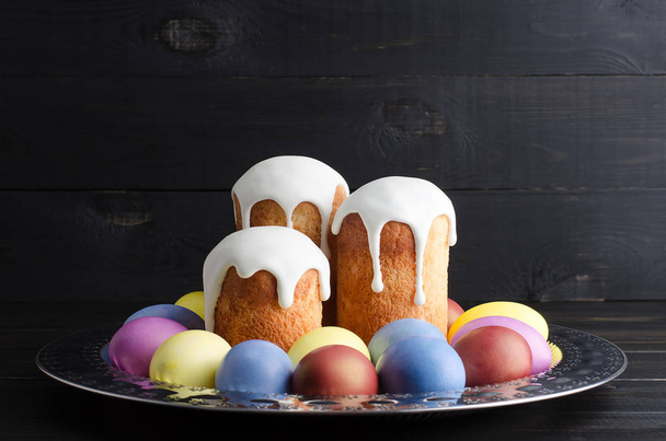 Easter still life on a dark, wooden background. Easter cakes with dyed chicken eggs on a platter - Photo, image