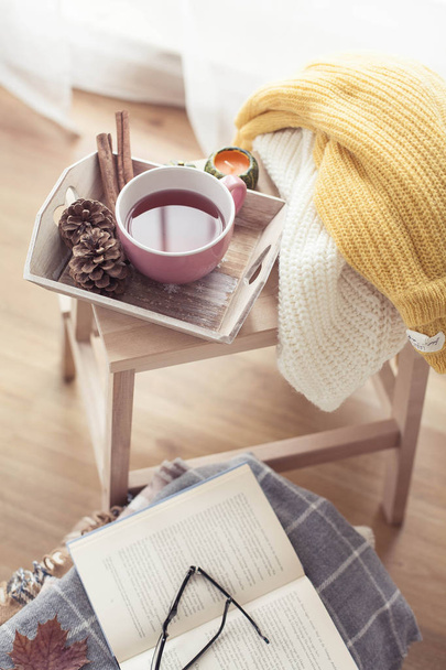 Knitted, warm sweaters, a cup of hot tea, autumn decor, a book, a pumpkin on a wooden chair. Cozy, autumn decor. Autumn interior, sofa. Fall. Winter. - Photo, Image
