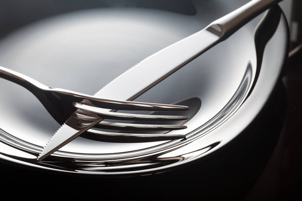Empty plate with shiny knife and fork on a black background. - Fotografie, Obrázek