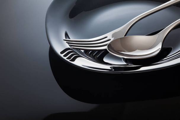 Empty plate with spoon and fork on a black background. - Foto, Bild
