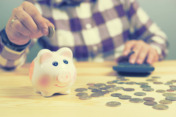 Man berekening van geld in munten aanbrengend piggy bank in kantoor - Foto, afbeelding