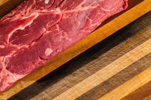 CLose up on fatty red uncooked steak sitting on scratched wooden cutting board with diagonal stripe pattern - 写真・画像