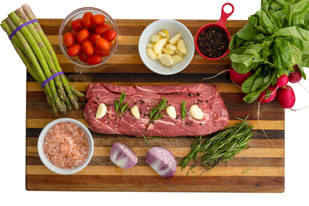 Bovenaanzicht van gekruid vlees naast groenten zoals tomaten en basilicum bladeren bovenop snijplank - Foto, afbeelding