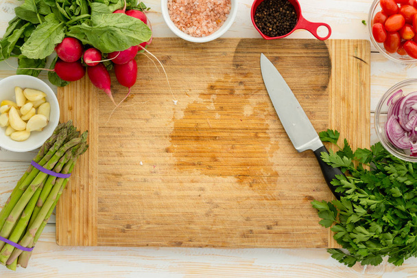 Yleisnäkymä puinen leikkuulauta ympäröi valikoituja vihanneksia kuten sipulia ja parsaa veitsellä
 - Valokuva, kuva