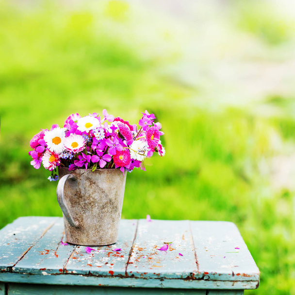 bouquet of colorful fresh wild flowers in metal jug on rustic wooden stool outdoors - Photo, image