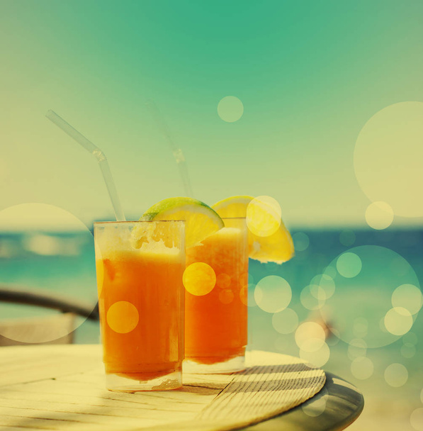 two glasses of tasty orange juice over table at beach - Photo, Image