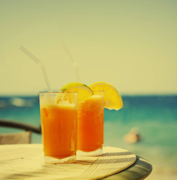 two glasses of tasty orange juice over table at beach - Fotoğraf, Görsel