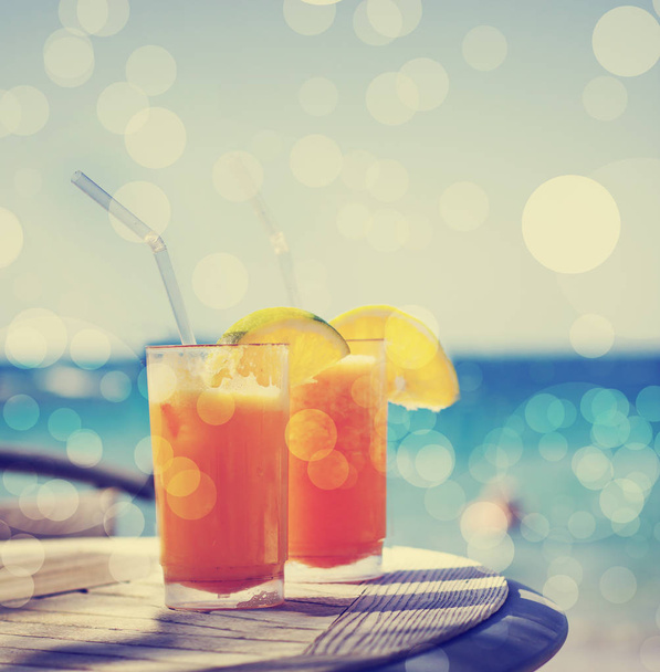 two glasses of tasty orange juice over table at beach - Foto, Imagem