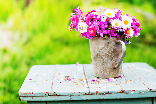bouquet of colorful fresh wild flowers in metal jug on rustic wooden stool outdoors - Photo, image