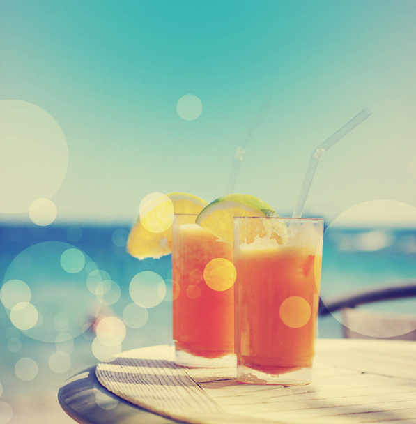 two glasses of tasty orange juice over table at beach - Photo, Image