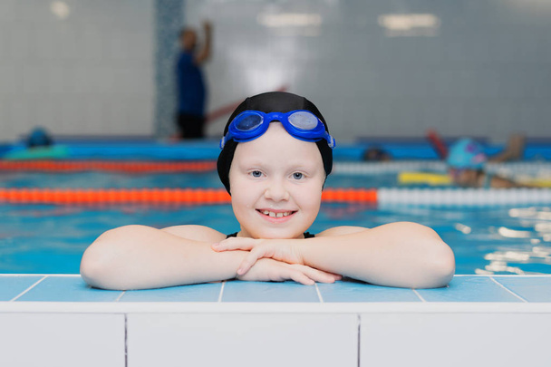 swimming lessons for children in the pool - portrait of a beautiful white-skinned girl in a bathing suit and swim cap - Photo, Image
