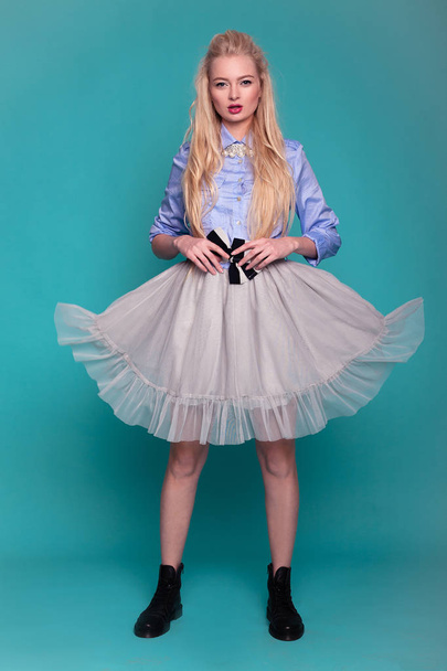 Blond model v průhledné šaty a černé boty pózuje v studio na modrém pozadí. - Fotografie, Obrázek