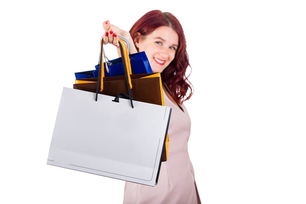 Excited young woman smiling with hand stretched forward holding paper shopping bags isolated over white background. - Photo, image