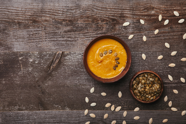 top view of bowls with delicious pumpkin soup and seeds on rustic wooden table - Foto, immagini