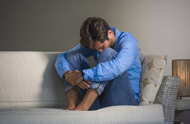 lifestyle portrait of young attractive and handsome sad latin man sitting tired and depressed at home sofa couch feeling overwhelmed and worried suffering depression crisis and anxiety problem - Fotografie, Obrázek