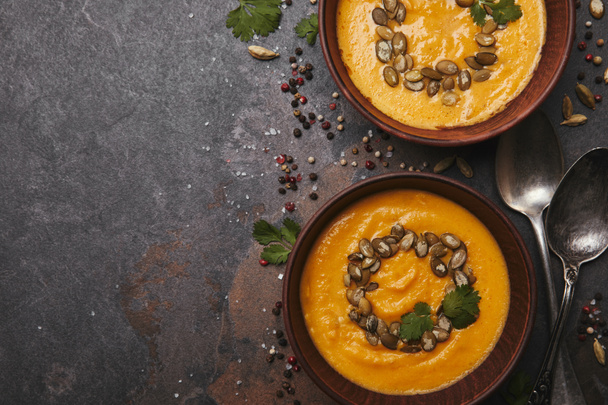 top view of tasty healthy pumpkin soup with seeds in bowls and spoons on dark surface - Fotografie, Obrázek