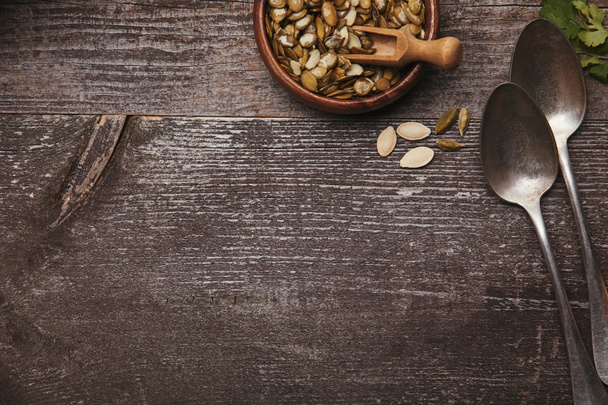 top view of bowl with pumpkin seeds and spoons on rustic wooden table - Fotoğraf, Görsel