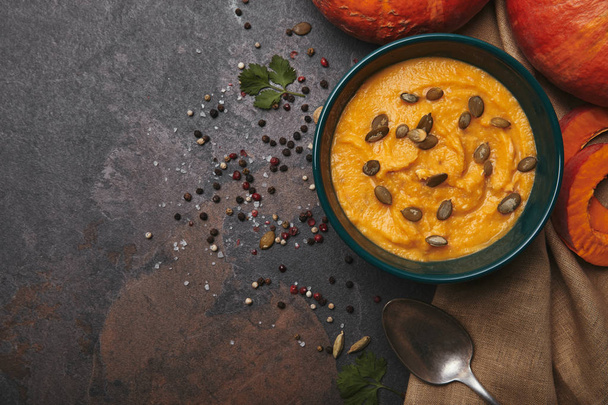 top view of delicious pumpkin soup in bowl, spoon, spices and fresh pumpkins on dark surface - Foto, imagen