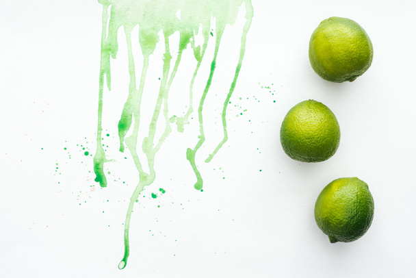 elevated view of whole limes on white surface with green watercolor - 写真・画像