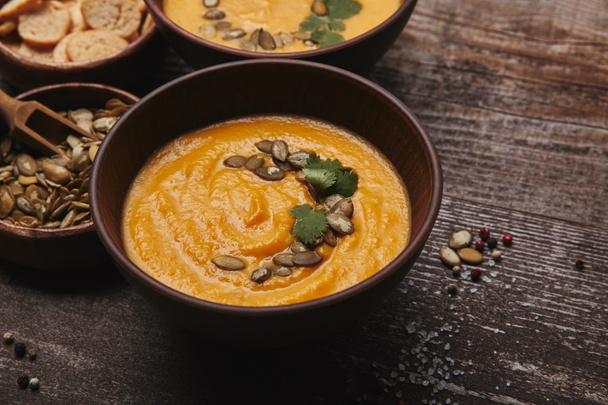 close-up view of gourmet pumpkin soup with pumpkin seeds and spices on wooden table  - Foto, Imagen