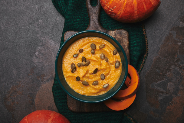 top view of healthy pumpkin soup in bowl and fresh pumpkins on dark surface  - Fotó, kép
