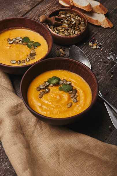 delicious pumpkin soup in bowls with spoons and sackcloth on wooden table  - Φωτογραφία, εικόνα