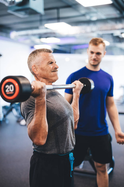 Senior Mann Gewichtheben, unterstützt von Personal Trainer. Altersvorsorge. Fitter Lebensstil. - Foto, Bild