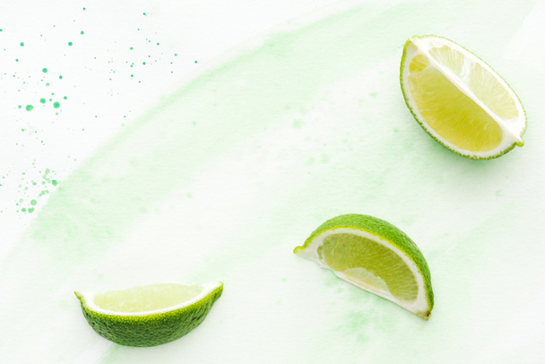 top view of pieces of yummy limes on white surface with green watercolor - Zdjęcie, obraz