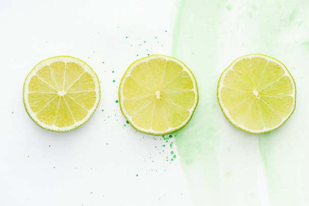 top view of three round pieces of ripe limes on white surface with green watercolor - Foto, imagen