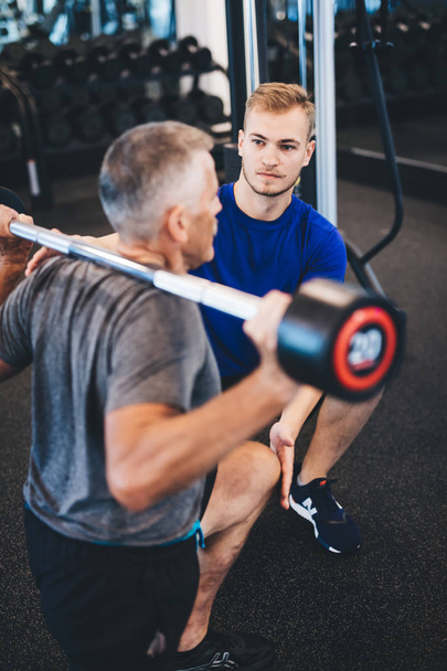 Personal trainer and senior man exercising at the gym. Gym assistant. Weightlifting. - Fotografie, Obrázek