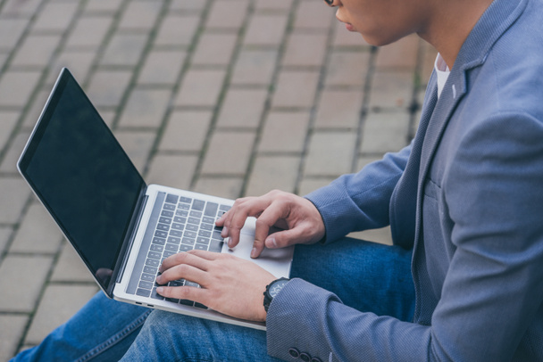 cropped view of teleworker using laptop while sitting on sidewalk - Foto, Imagem