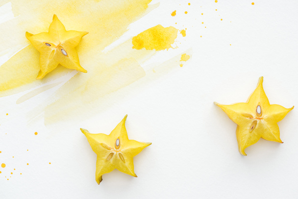 vista superior de tres frutos estelares maduros en superficie blanca con acuarela amarilla
 - Foto, Imagen