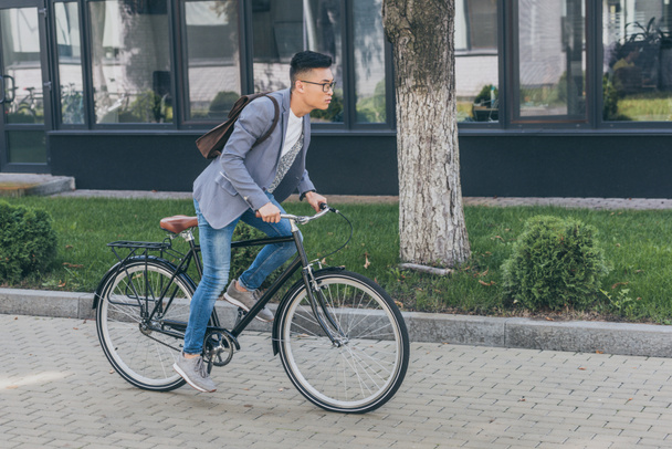 asian man with leather backpack cycling on bicycle in city - Zdjęcie, obraz