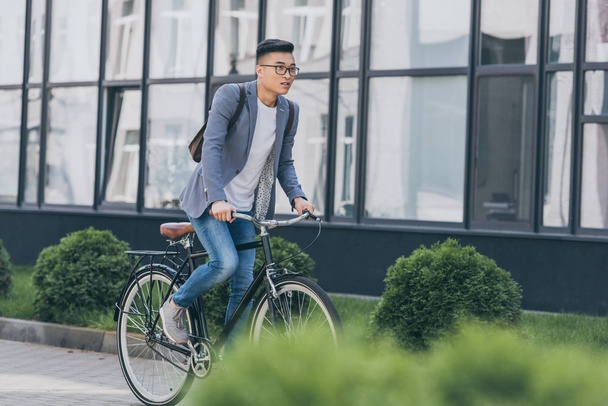stylish asian man in gray jacket biking in city - Foto, imagen