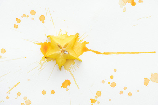 vue surélevée du fruit étoilé jaune sur la surface blanche avec éclaboussures de peinture jaune
 - Photo, image