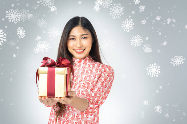 Photo of asian curious woman in red dress enjoy new year gift box. Young woman holding gift  box with red bow being excited and surprised  holiday present isolated white background and snowflake. - Фото, изображение