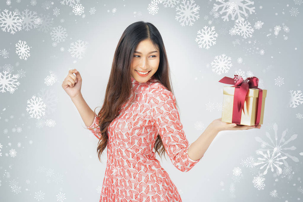 Photo of asian curious woman in red dress enjoy new year gift box. Young woman holding gift  box with red bow being excited and surprised  holiday present isolated white background and snowflake. - Zdjęcie, obraz