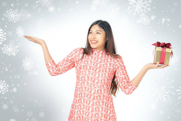 Photo of asian curious woman in red dress enjoy new year gift box. Young woman holding gift  box with red bow being excited and surprised  holiday present isolated white background and snowflake. - Valokuva, kuva