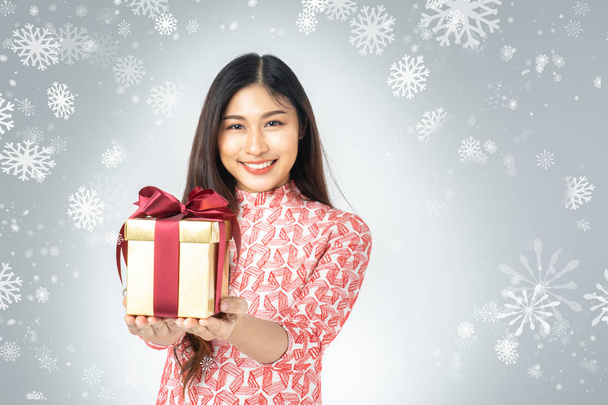Photo of asian curious woman in red dress enjoy new year gift box. Young woman holding gift  box with red bow being excited and surprised  holiday present isolated white background and snowflake. - Foto, imagen