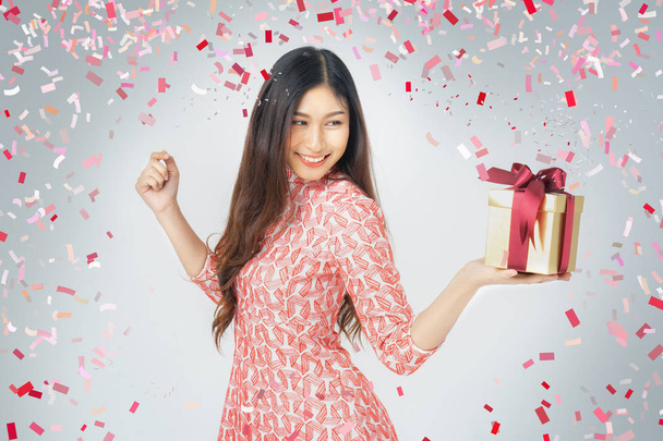 Photo of asian curious woman in red dress rejoicing her birthday or new year gift box. Young woman holding gift  box with red bow being excited and surprised  holiday present isolated white background - Foto, imagen