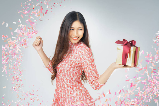 Photo of asian curious woman in red dress rejoicing her birthday or new year gift box. Young woman holding gift  box with red bow being excited and surprised  holiday present isolated white background - Foto, afbeelding