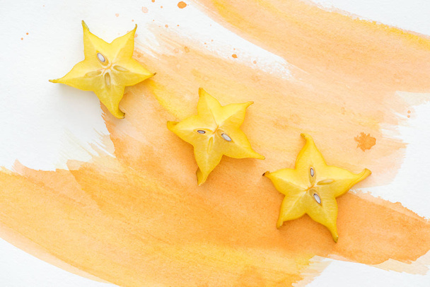 top view of sweet exotic star fruits on white surface with orange watercolor - Photo, Image