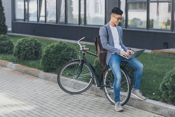 elegante asiatico freelancer utilizzando laptop mentre seduto su bicicletta
 - Foto, immagini