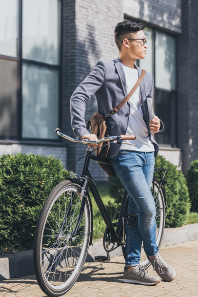 stylish asian man with laptop and leather bag leaning on bicycle - Fotoğraf, Görsel